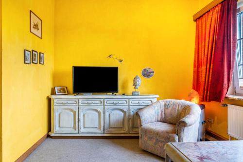 a yellow living room with a tv and a chair at Gästehaus Ziegler in Neuenkirchen
