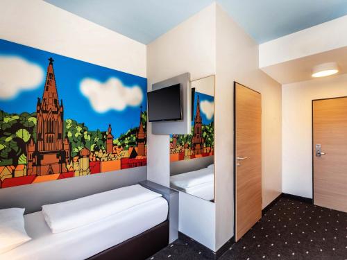 a room with two beds and a tv on the wall at B&B Hotel Freiburg-Süd in Freiburg im Breisgau