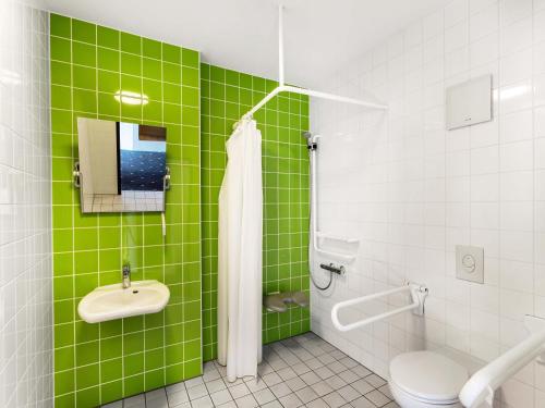a green tiled bathroom with a toilet and a sink at B&B Hotel Freiburg-Süd in Freiburg im Breisgau