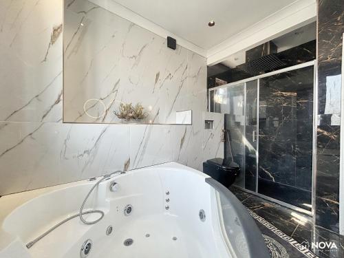 Una bañera blanca en un baño con ducha. en Elegant 6 bedroom Family Home, 2x corner Jacuzzi bath in LUTON, en Luton