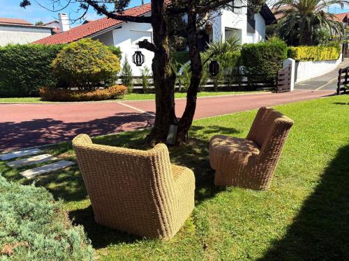 twee rieten stoelen in het gras bij een boom bij Chambre confort - Le Boudoir in Hendaye