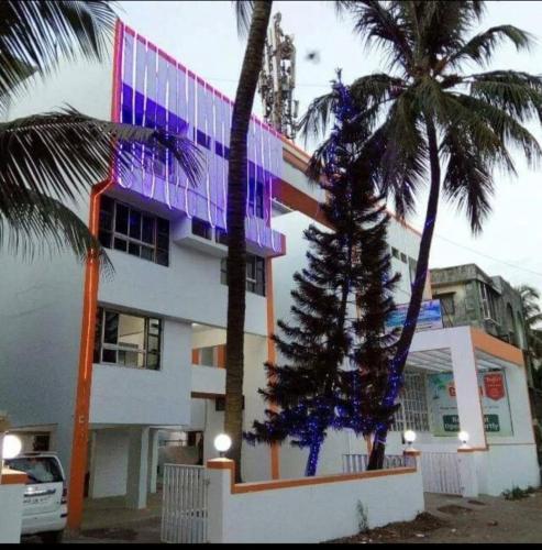 a building with a palm tree in front of it at Hotel Guruji in Alibag