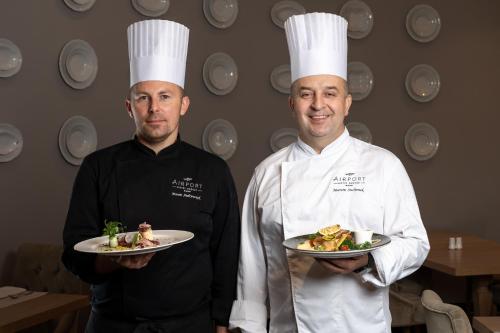 two chefs standing in a kitchen holding plates of food at Airport Hotel Okęcie in Warsaw