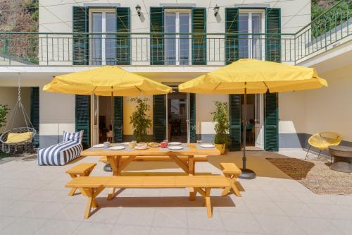 a patio with two tables and two yellow umbrellas at Maria Madalena in Madalena do Mar