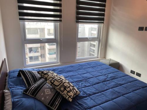 a bedroom with a blue bed with two pillows and two windows at Dpto Económico a 6 min de Plaza Ñuñoa in Santiago