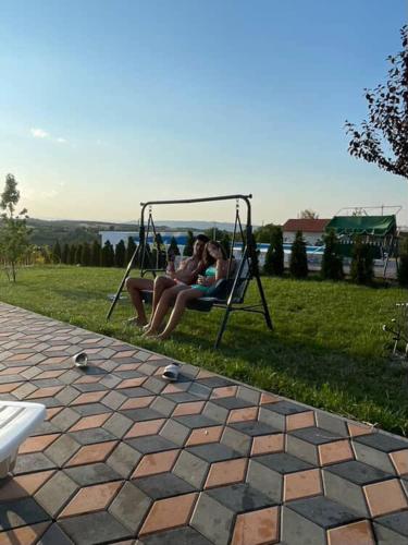 two women sitting on a swing in a yard at Vikendica sa bazenom Čarolija Kruševac in Kruševac