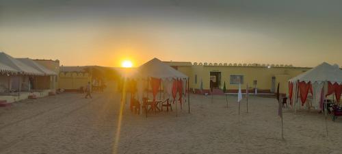a beach with tables and umbrellas and the setting sun at Melody Moon Desert Camp & Resort in Jaisalmer