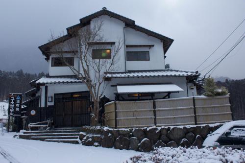 a white house with snow on the ground at Yufuin Country Road Youth Hostel in Yufuin