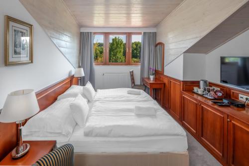 a bedroom with a white bed and a television at Bakony Resort - a Felnőttbarát Hotel - Szarvaskút Vendégpark in Zirc