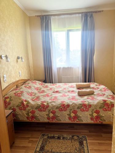 a bedroom with a bed with a floral bedspread and a window at Гармонія in Skhidnitsa