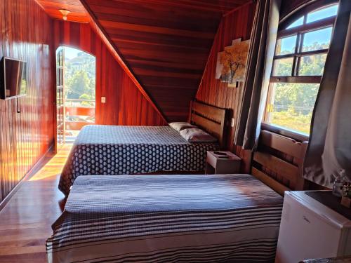 two beds in a room with wooden walls and windows at Casa do Trem Suítes in Campos do Jordão