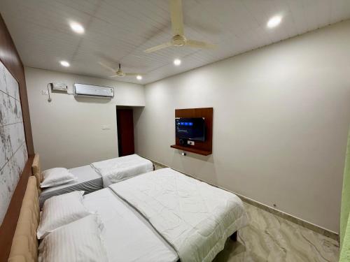 a bedroom with two beds and a tv on the wall at Kanasu Residency in Malpe