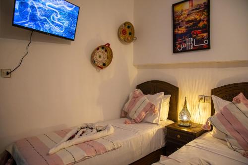 a bedroom with two beds and a tv on the wall at Riad Hikaya - Fes Story in Fès
