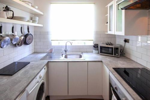 a white kitchen with a sink and a microwave at Newly Refurbished - Margate Sunset Retreat in Margate