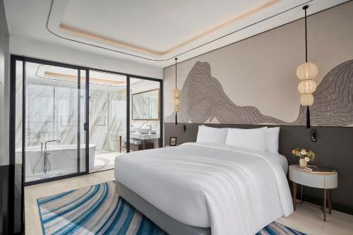 a bedroom with a large white bed and a bathroom at voco Ma Belle Danang by IHG in Da Nang