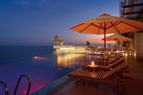 a pool with tables and umbrellas next to the water at voco Ma Belle Danang by IHG in Da Nang