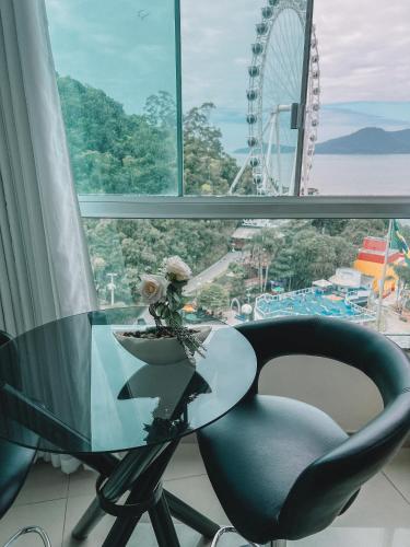 a glass table and a chair in front of a window at Loft vista panorâmica da Roda gigante e orla de BC in Balneário Camboriú