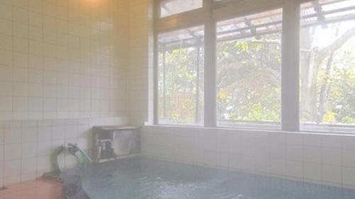 a bathroom with a hot tub and a window at Kanesada Ryokan in Kuroishi
