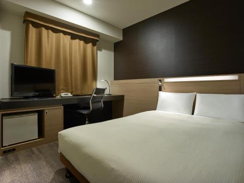 a hotel room with a bed and a desk with a television at Mitsui Garden Hotel Okayama in Okayama