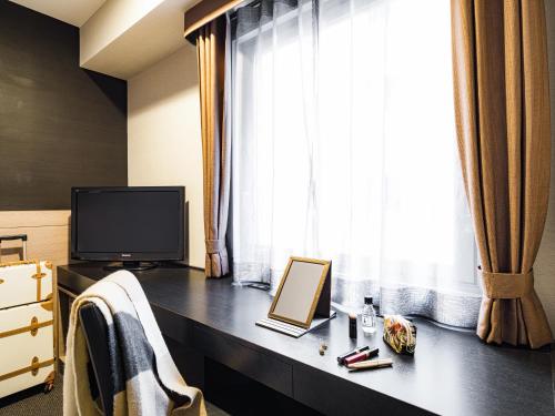 a room with a desk with a tv and a window at Mitsui Garden Hotel Okayama in Okayama