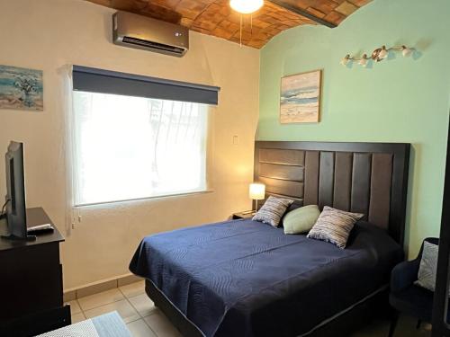 a bedroom with a bed with a blue comforter and a window at Le Petit Oasis a few steps from the Beach in Peñita de Jaltemba