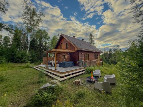 une cabane en rondins avec une terrasse dans un champ dans l'établissement Sara Chalet With Spa Hiking Trails, à Notre-Dame-de-la-Merci