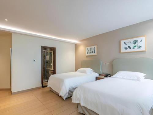 two beds in a hotel room with white sheets at Leisurely Hotel Shenzhen in Shenzhen