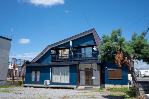 a blue house with a balcony and a tree at KAMUI Stay in Asahikawa