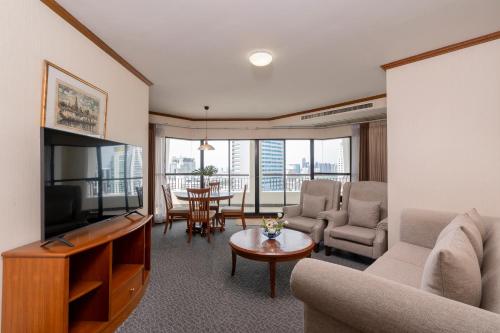a living room with a couch and a television and a table at Grand Diamond Suites Hotel in Bangkok
