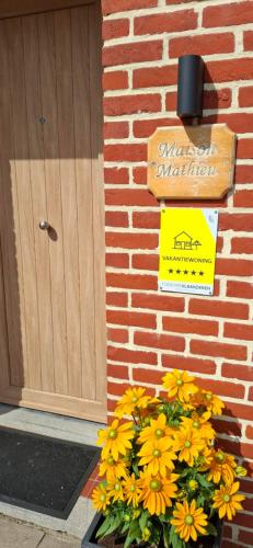 a sign in front of a brick building with yellow flowers at Maison Mathieu in Bilzen