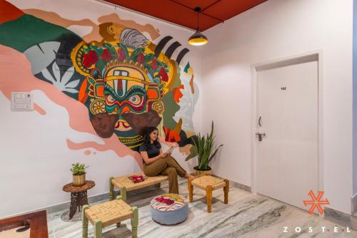a woman sitting on a couch in front of a mural at Zostel Chennai, Anna Nagar in Chennai
