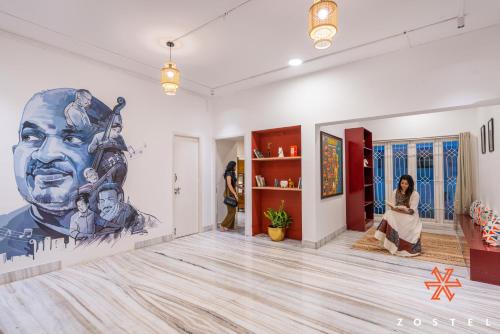 a woman sitting in a room with a large painting on the wall at Zostel Chennai, Anna Nagar in Chennai