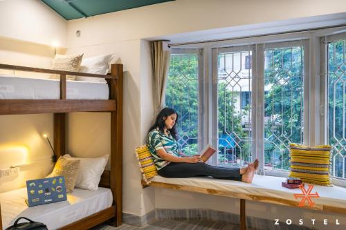 a woman sitting on a bunk bed reading a book at Zostel Chennai, Anna Nagar in Chennai