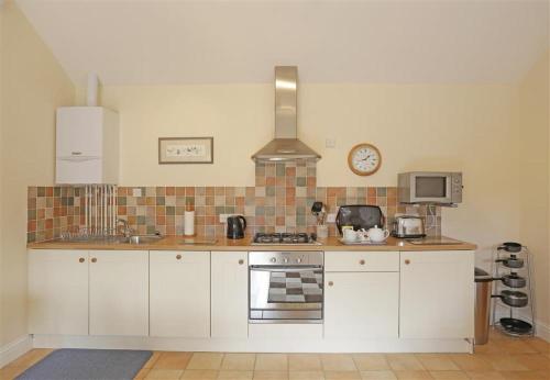 a kitchen with white cabinets and a clock on the wall at The Tack Room in Wangford