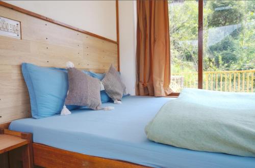 a bedroom with a bed with blue pillows and a window at Jaadooghar Rainbow Farms in Mussoorie
