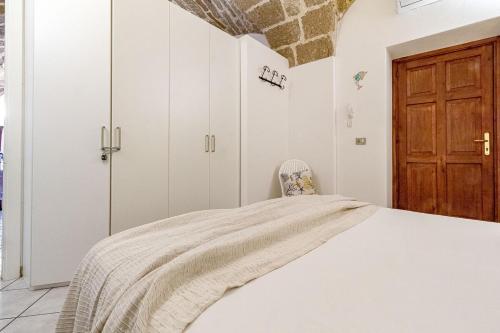 a white bedroom with a bed and a wooden door at Nura's - Il Nido central old town Bastioni view in Alghero