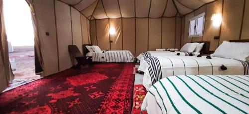 a room with three beds and a red carpet at Sahara Elegance Camp in Merzouga