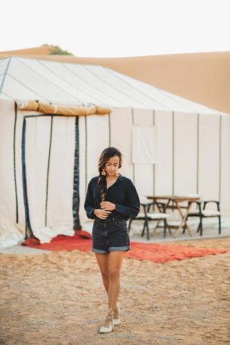 a woman is standing in front of a tent at Erg Chebbi Dunes Desert Camp in Merzouga