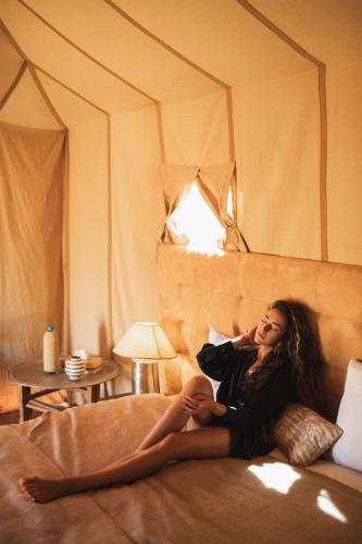 a woman sitting on a bed in a room at Erg Chebbi Dunes Desert Camp in Merzouga