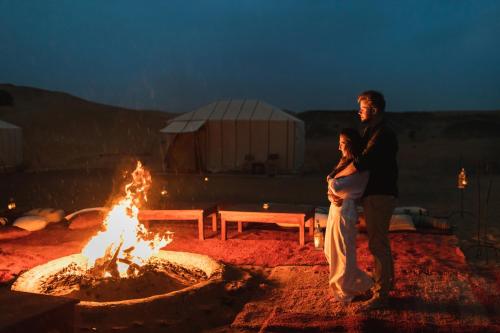 a man and a woman standing in front of a fire at Erg Chebbi Dunes Desert Camp in Merzouga
