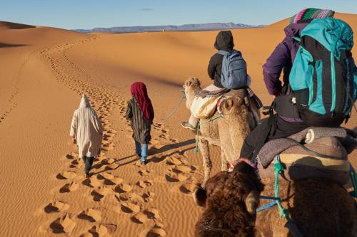 a group of people riding camels in the desert at Erg Chebbi Dunes Desert Camp in Merzouga