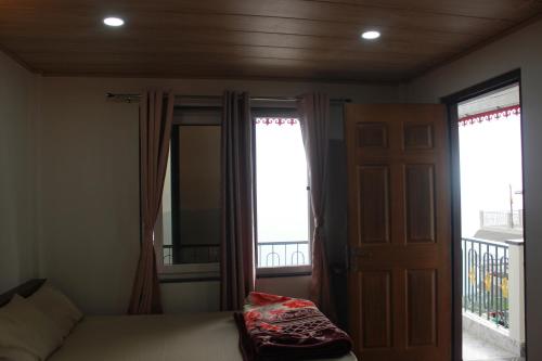 a bedroom with a bed and two windows and a door at Nijung Homestay, Dowhill in Kurseong