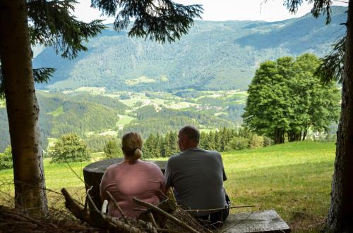 a man and woman sitting on a bench looking at a valley at Koča v Lozah in Gornji Grad