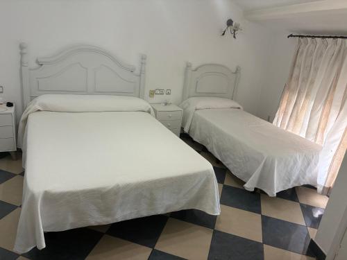 two beds in a room with a checkered floor at Hostal Restaurante La Niña in Palos de la Frontera