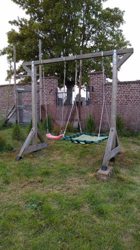 a swing set in a yard with a brick wall at Luxe loft in vierkantshoeve in Sint-Truiden
