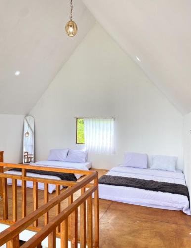 two beds in a room with white walls and wooden floors at Warm kabin dieng in Dieng