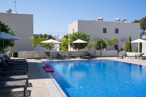 a swimming pool with chairs and umbrellas next to a building at Protaras The Icon 001 at Mythical Seas in Paralimni