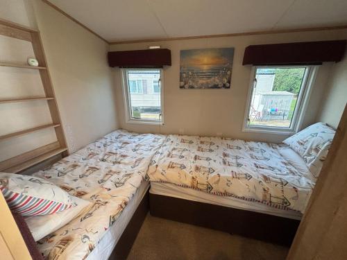a small bedroom with two beds and two windows at Oak Village 64 - Grange Leisure disability caravan - pet friendly, wifi and ramped decking in Mablethorpe