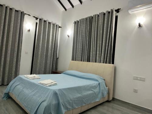 a bedroom with a bed with blue sheets and curtains at Villa J&T in Katunayake