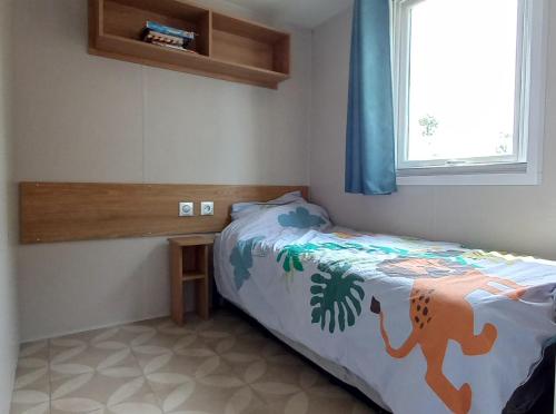 a small bedroom with a bed with a dinosaur blanket at En bord d'eau - charmant Mobil-home climatisé - Cap ferret in Lège-Cap-Ferret